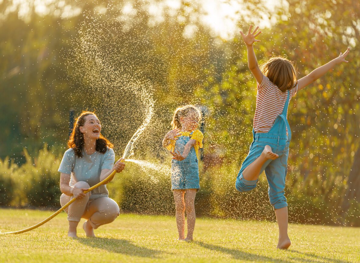 children and their mother playing with the water hose in the backyard